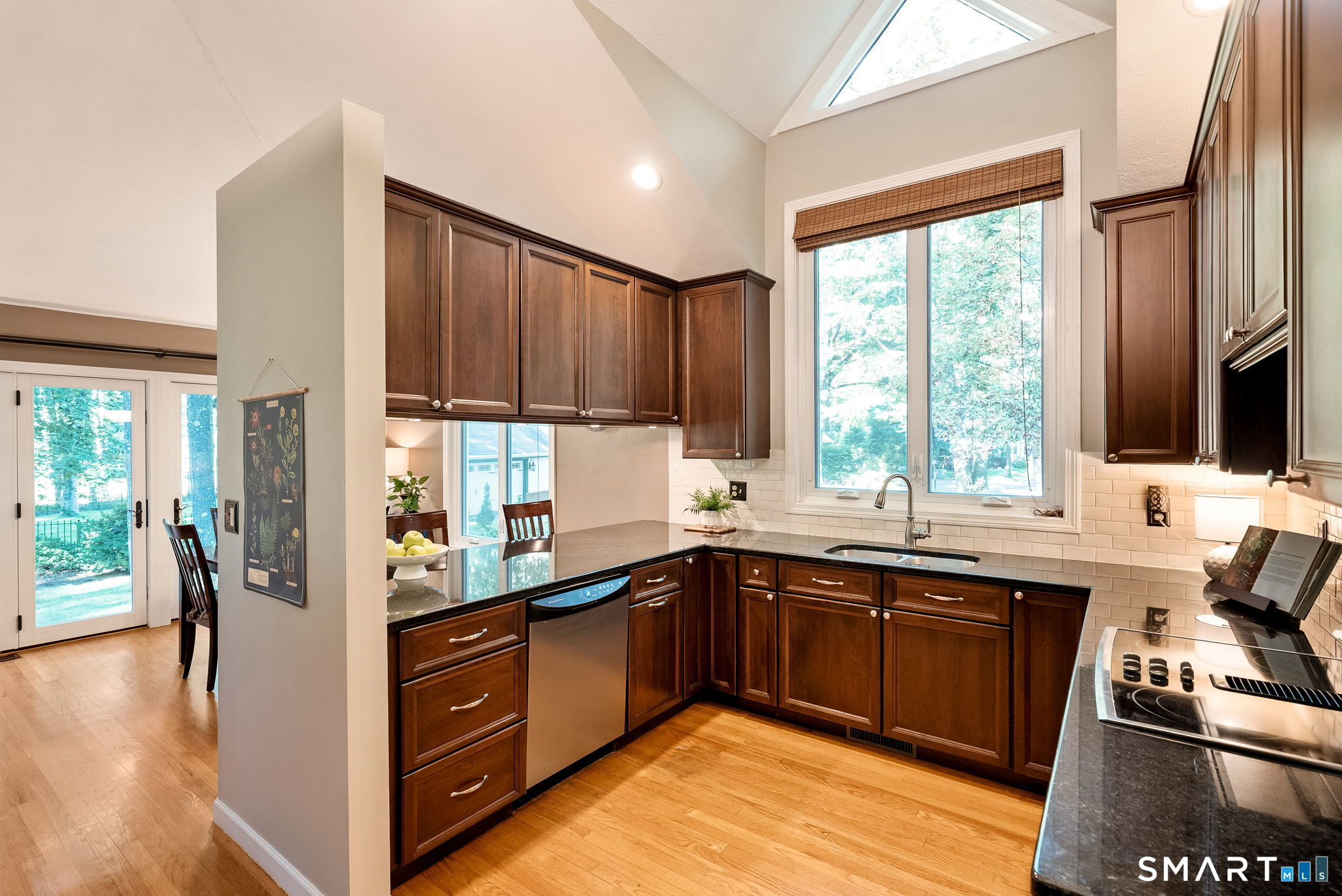 Kitchen with dark wood cabinets, granite counters, stainless steel appliances, and a tall window.