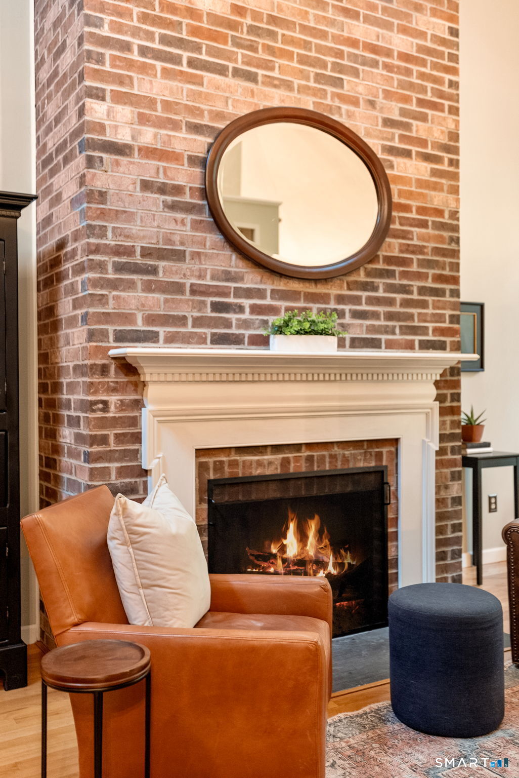 Living room fireplace with a red brick surround, round mirror, and leather chair.