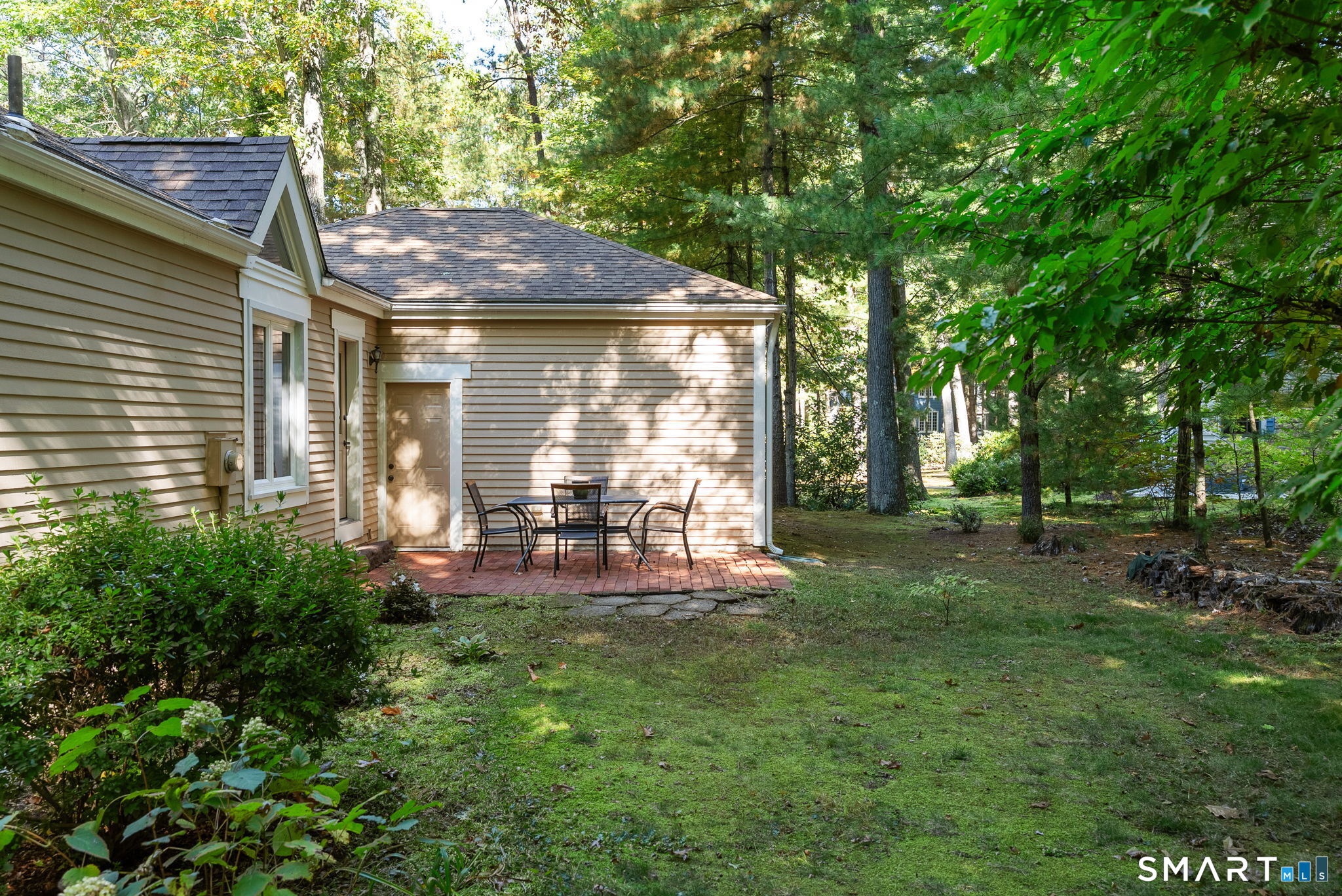 Home’s wooded backyard with a brick patio and outdoor dining set.