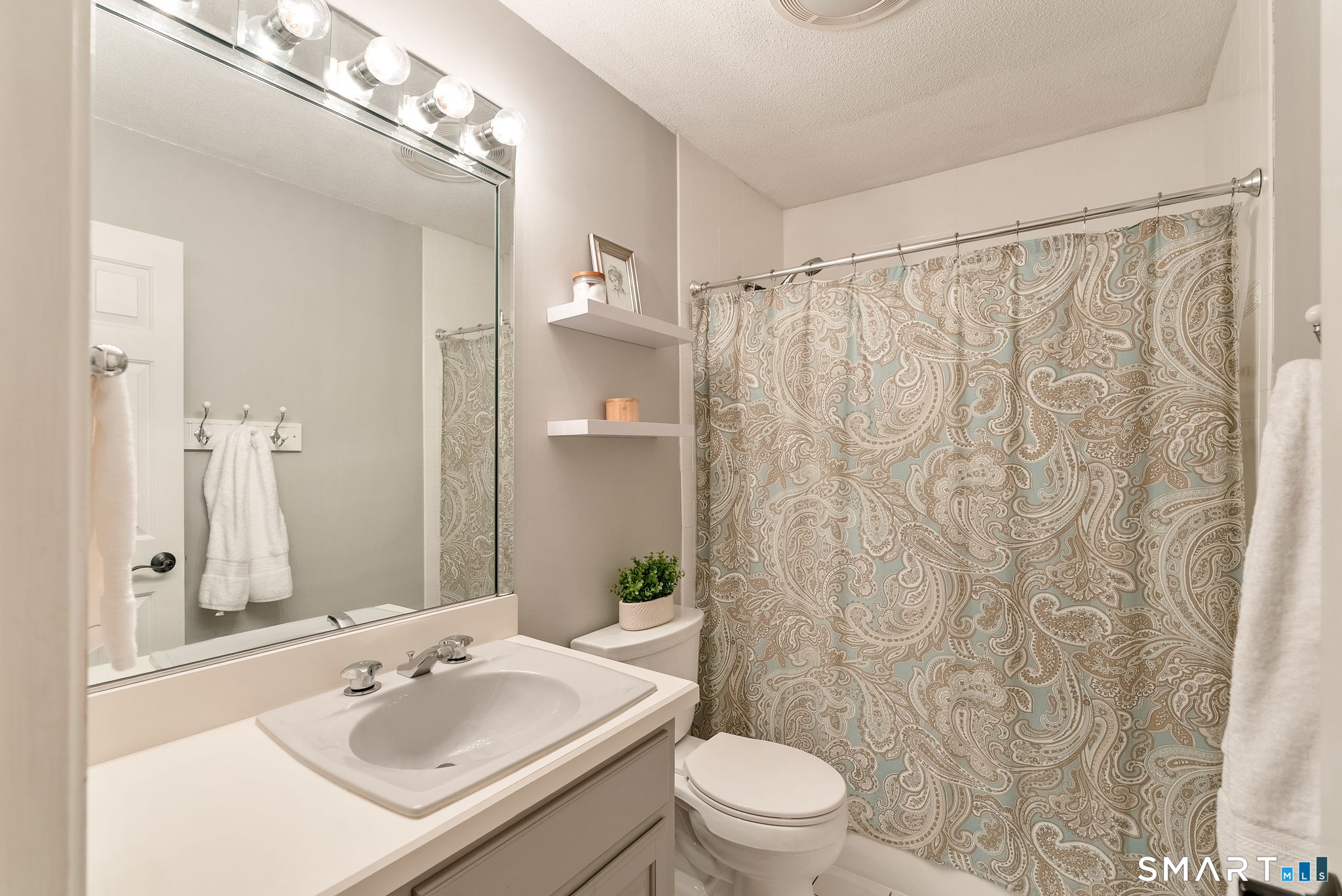 Bathroom with a white vanity and large mirror beside a paisley-patterned shower curtain.