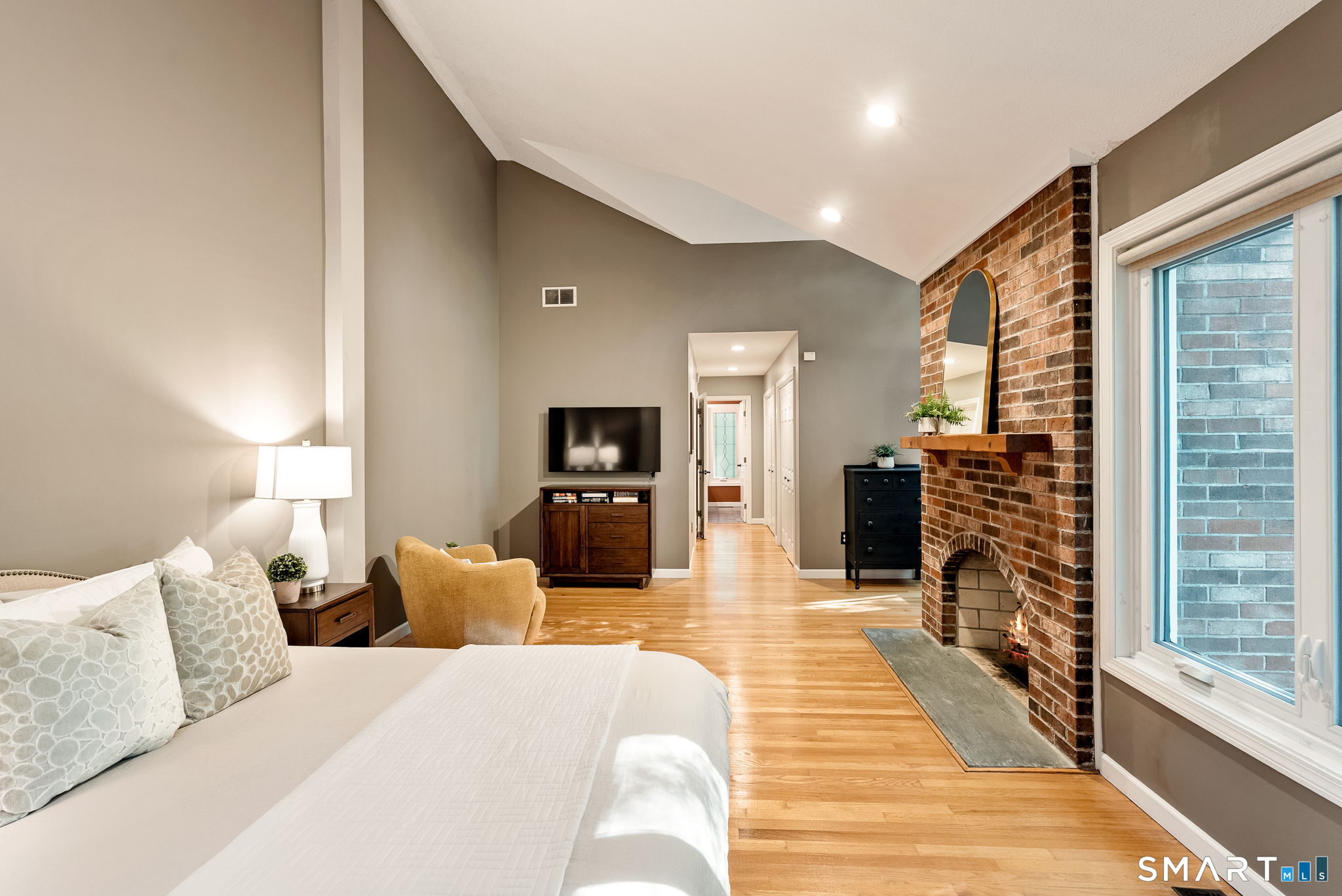 Furnished bedroom with a vaulted ceiling, brick fireplace, hardwood floors, and sitting area.