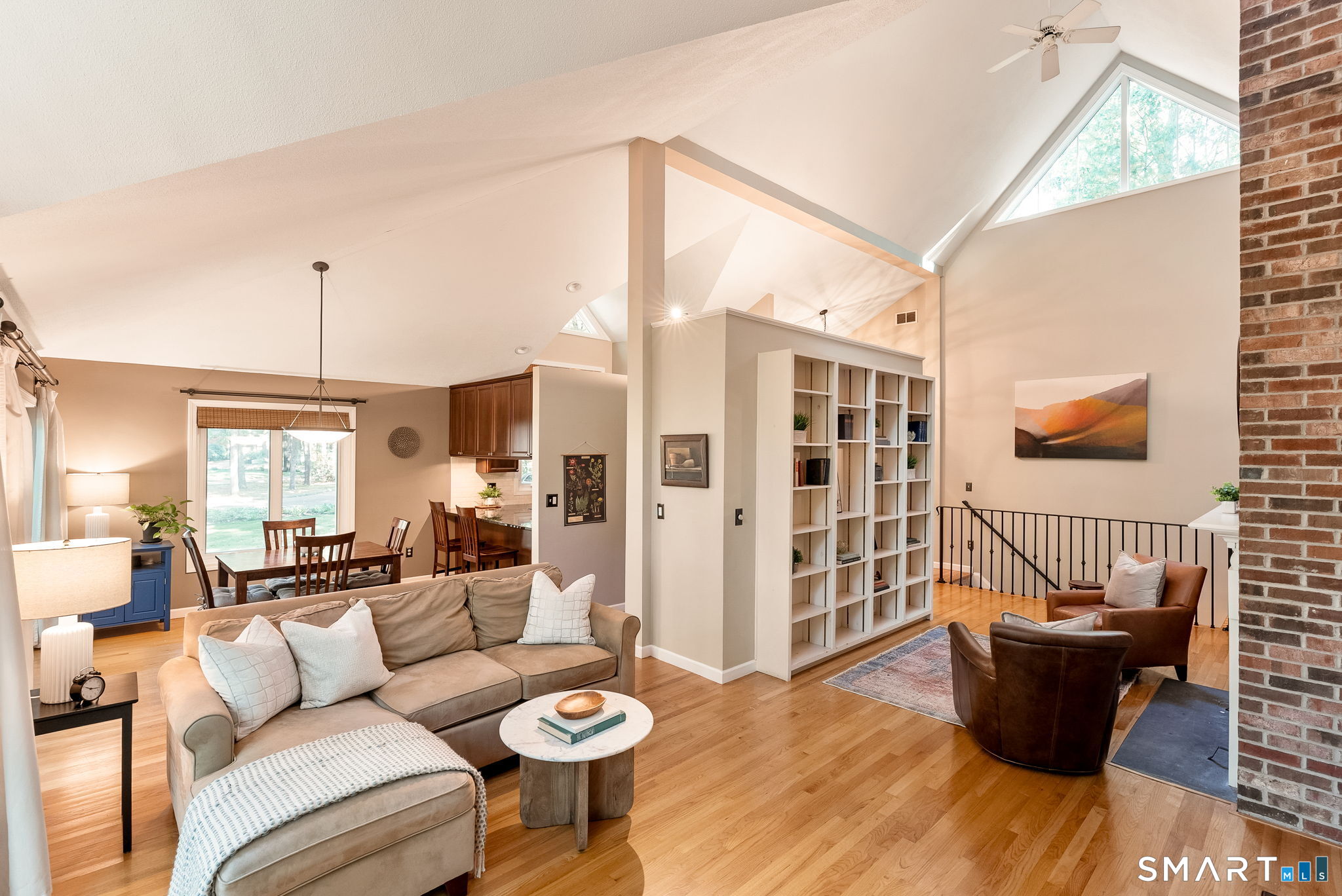 Open living room with vaulted ceiling, built-in shelving, brick fireplace, and dining area.