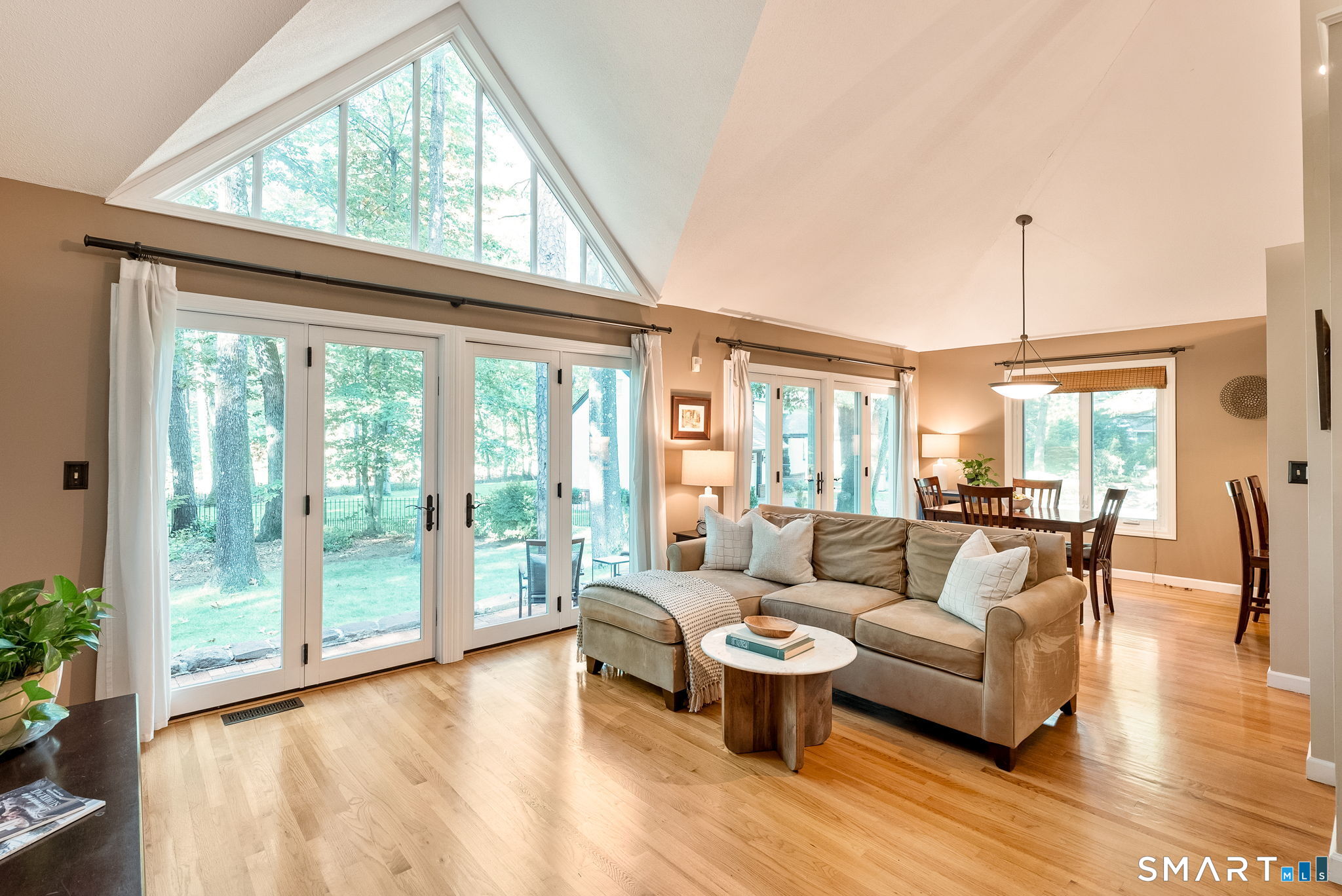 Living room with vaulted ceiling, triangular clerestory window, hardwood floors, and glass doors to the yard.