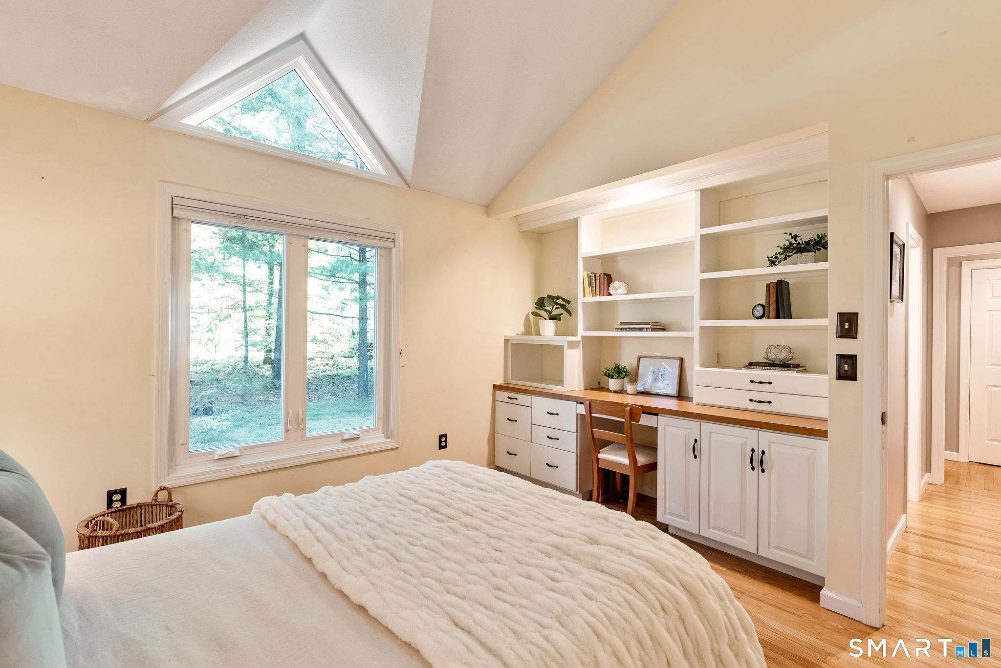 Bedroom with built-in desk and bookshelves beneath a vaulted ceiling and triangular skylight.