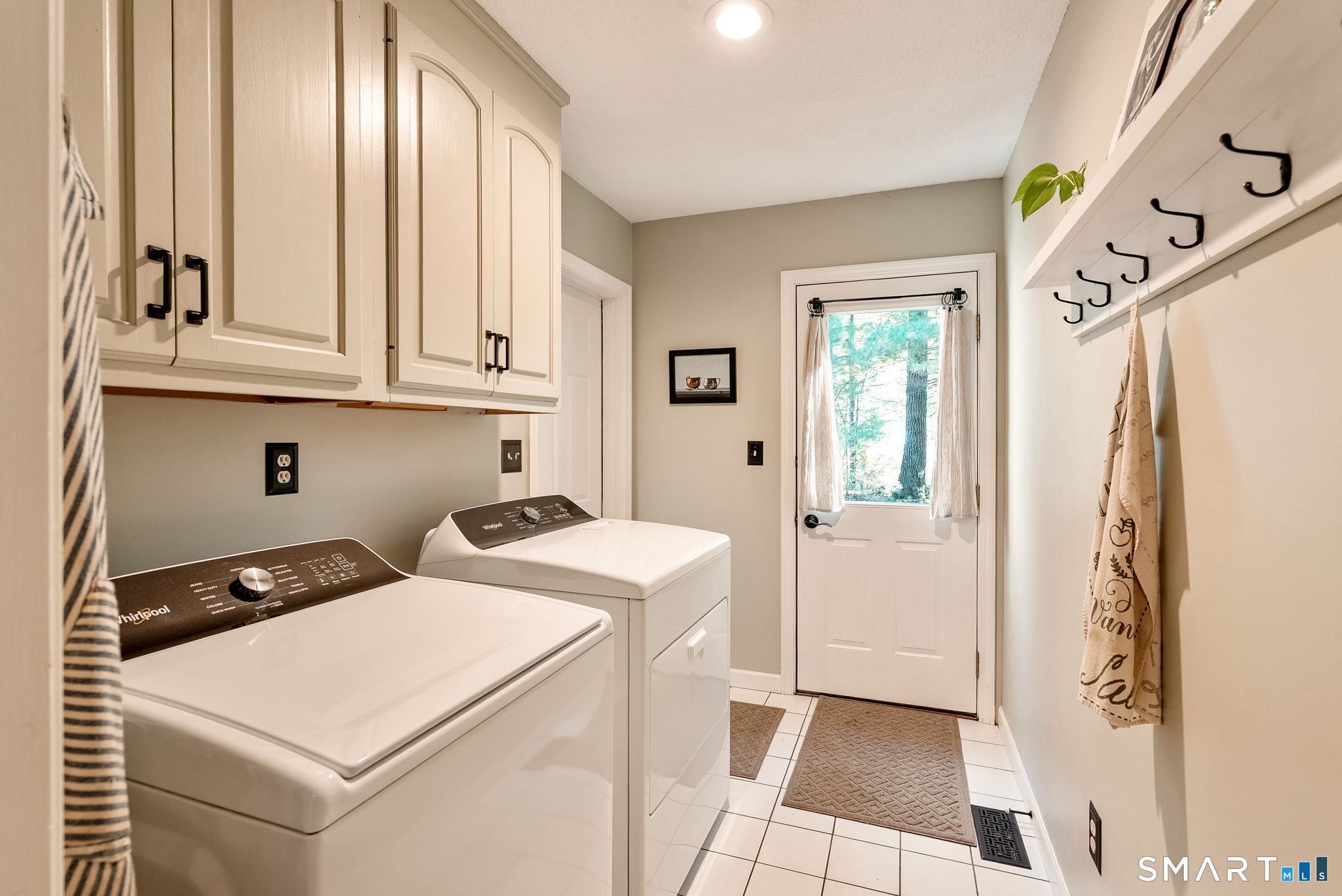 Laundry room with white washer and dryer, overhead cabinets, and a glass-paneled door.
