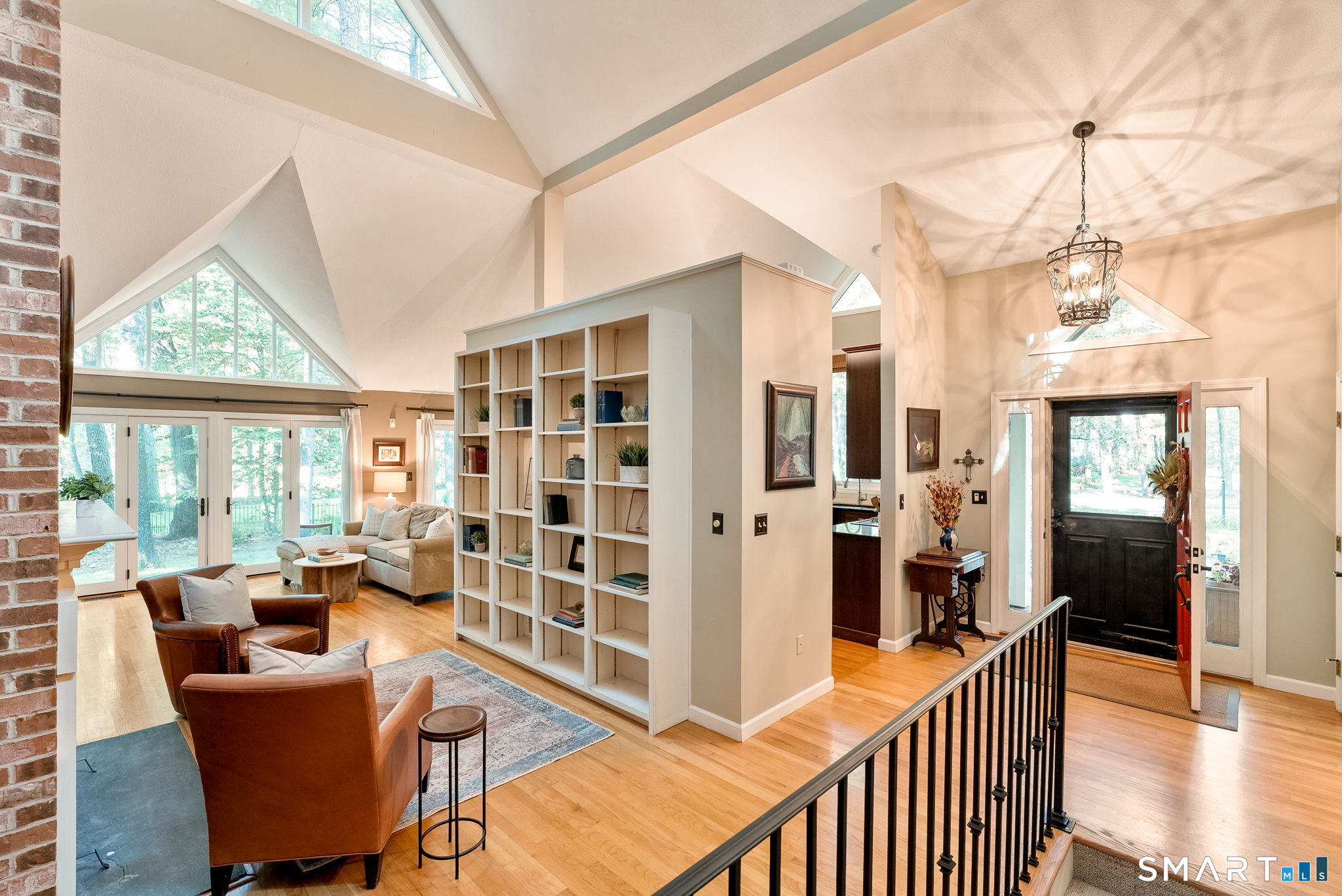 Vaulted living room with built-in bookshelves, triangular windows, hardwood floors, and seating beside the entry.
