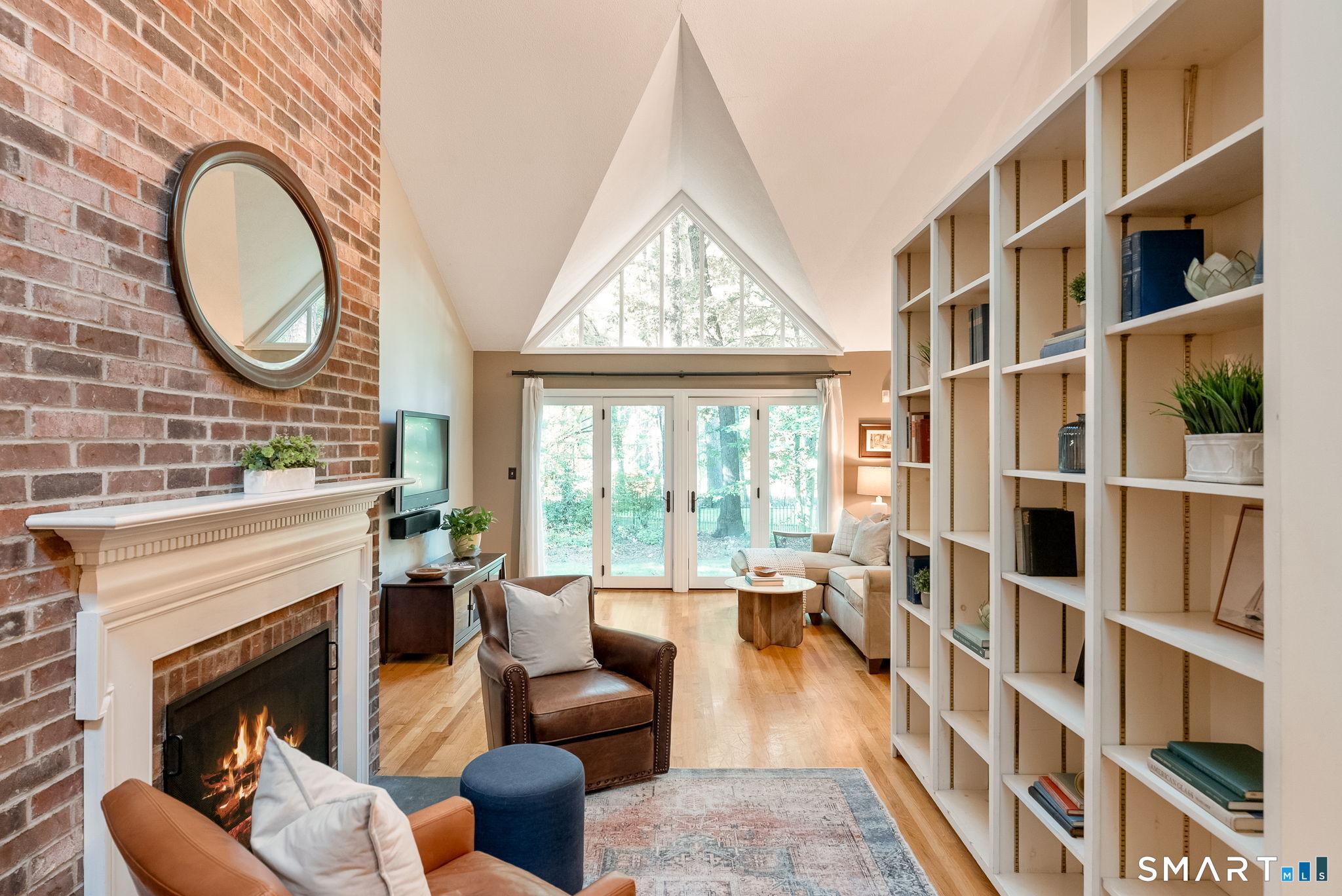Living room with brick fireplace, floor-to-ceiling shelves, vaulted ceiling, and a triangular window.