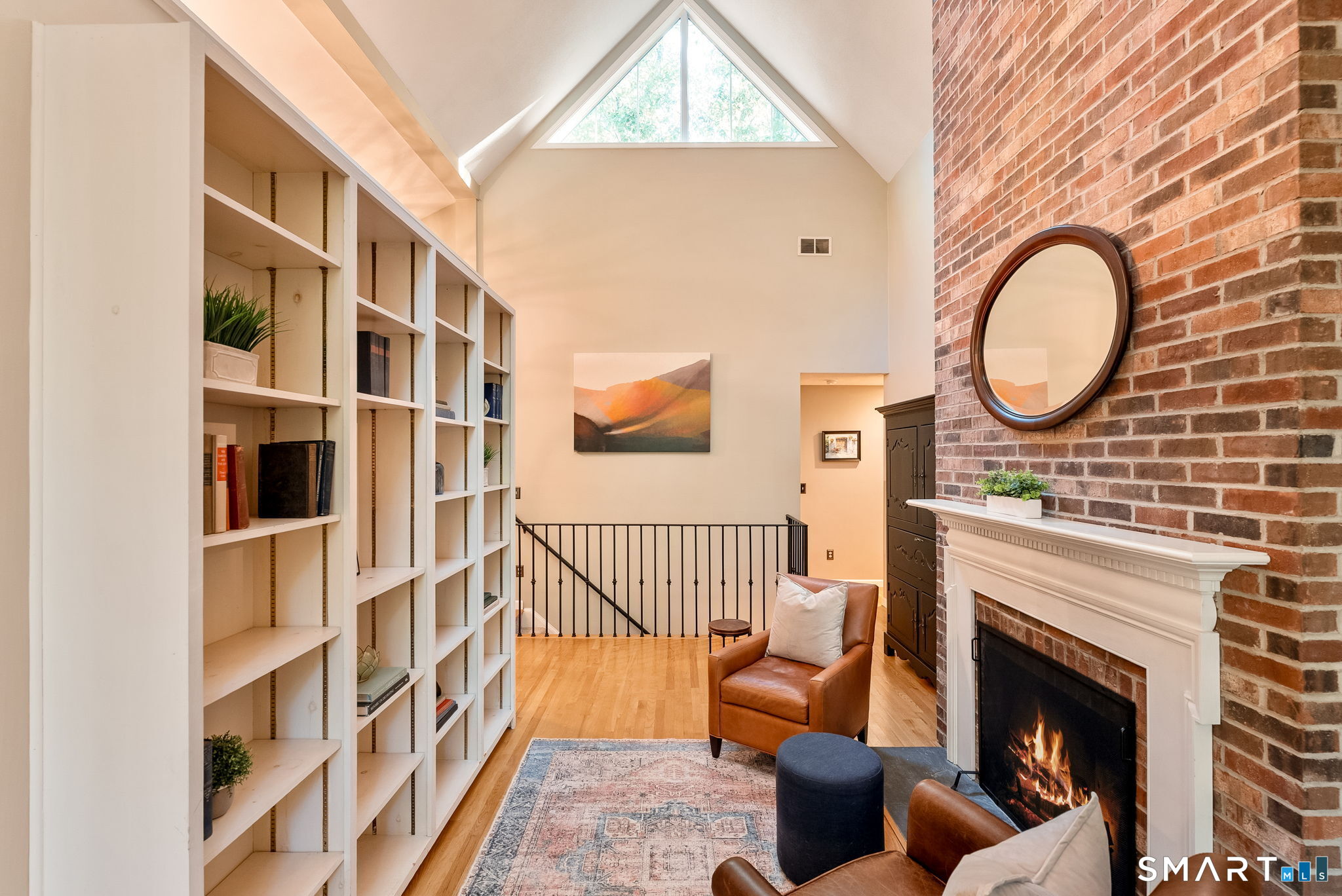 Sitting area with built-in bookshelves, a brick fireplace, and a vaulted ceiling with triangular window.
