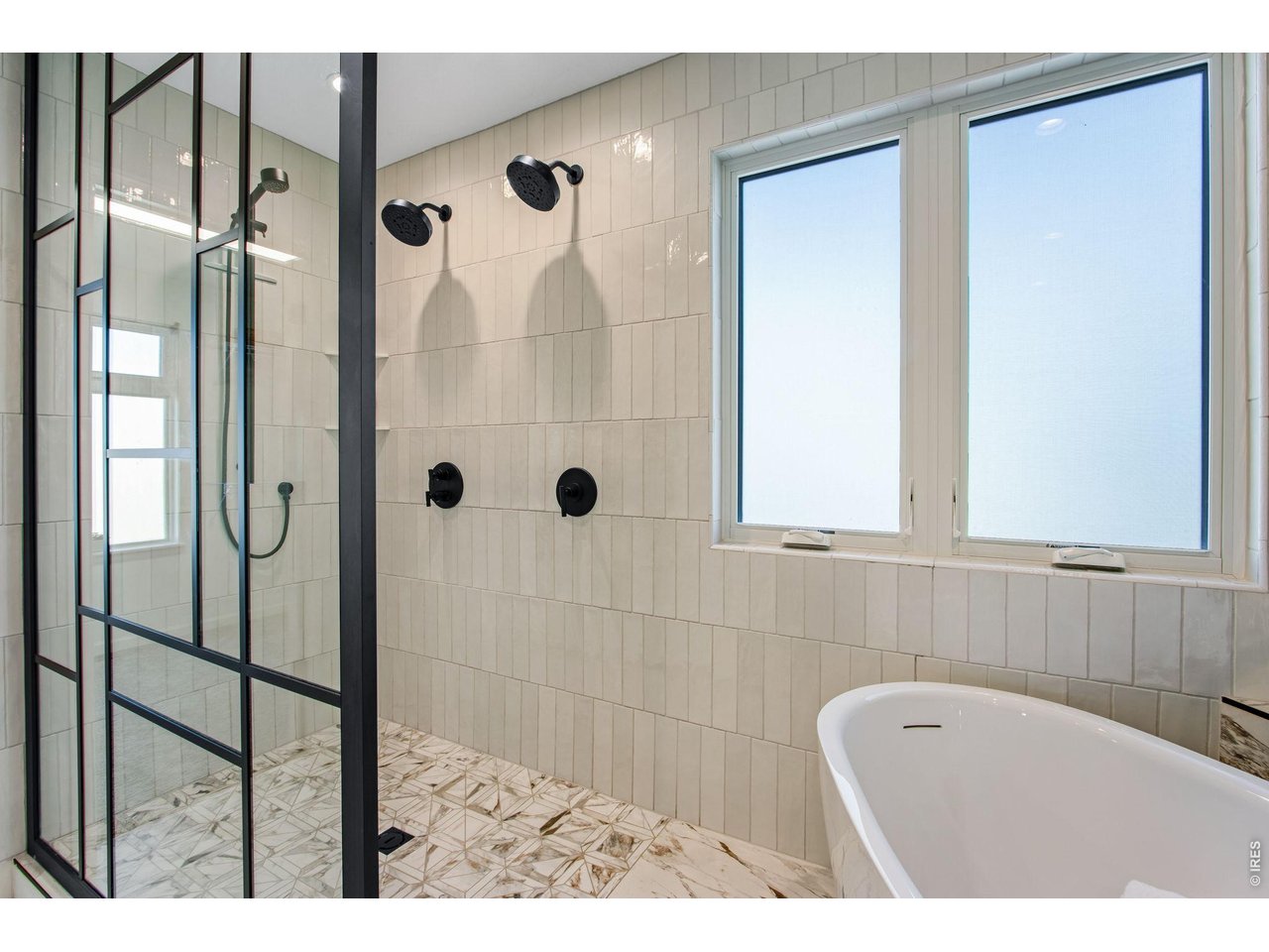 Bathroom with a freestanding soaking tub and black-framed walk-in shower with dual showerheads.
