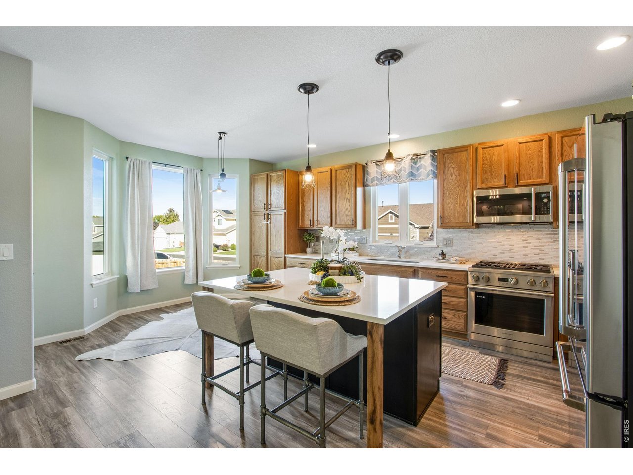 Kitchen with a large white island, upholstered stools, wood cabinetry, and stainless steel appliances.