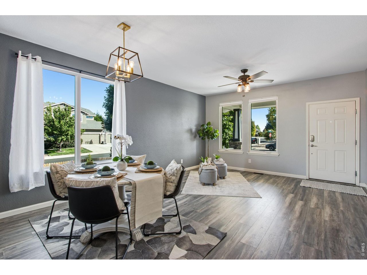 Dining area with a set table, large curtained window, and adjoining entry sitting area.