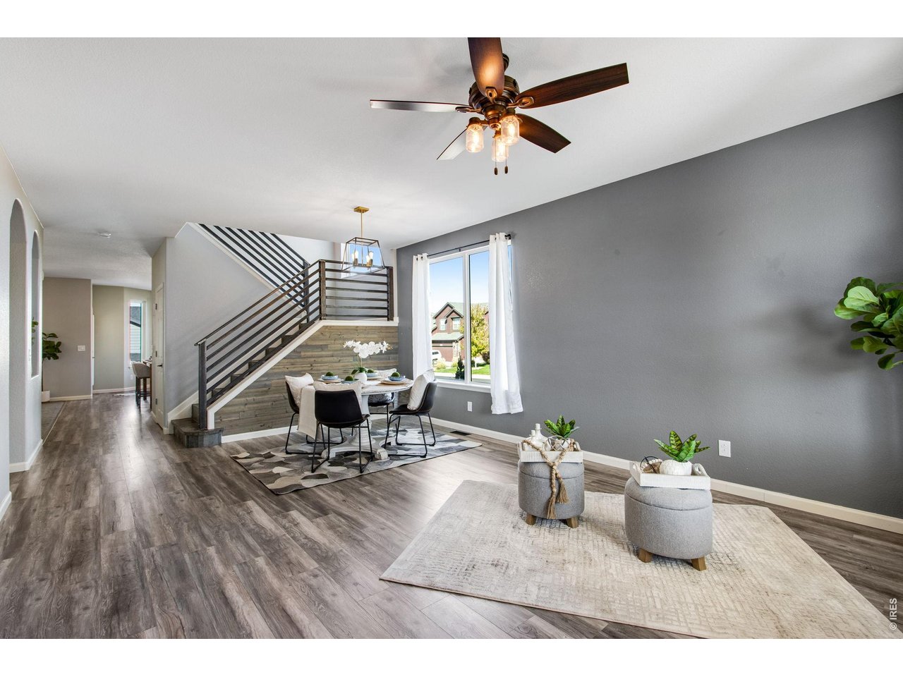 Open-plan living and dining room with a metal-railed staircase and large window.
