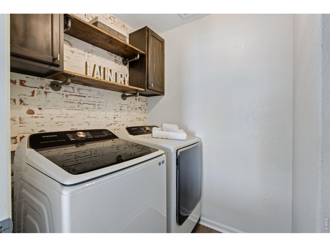Laundry room with washer and dryer, rustic brick backsplash, and dark wood cabinets.