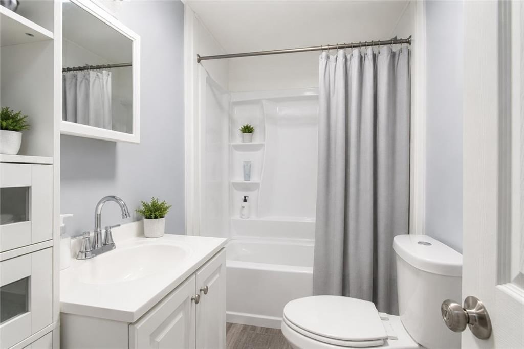 Bright bathroom with a white vanity, bathtub behind a gray curtain, and white toilet.