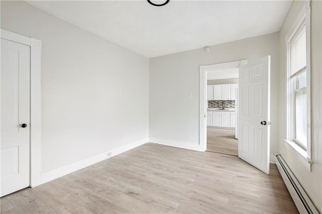 Empty room with light wood-look flooring, a window, and an open doorway to the kitchen.