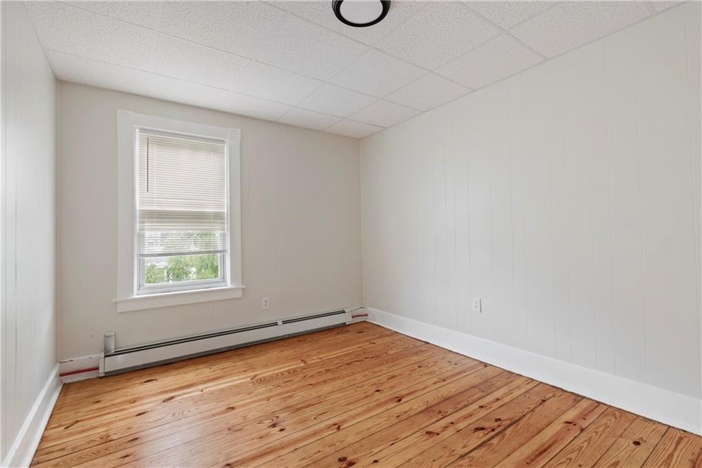Empty room with wood plank flooring, white paneled walls, and a window with blinds.