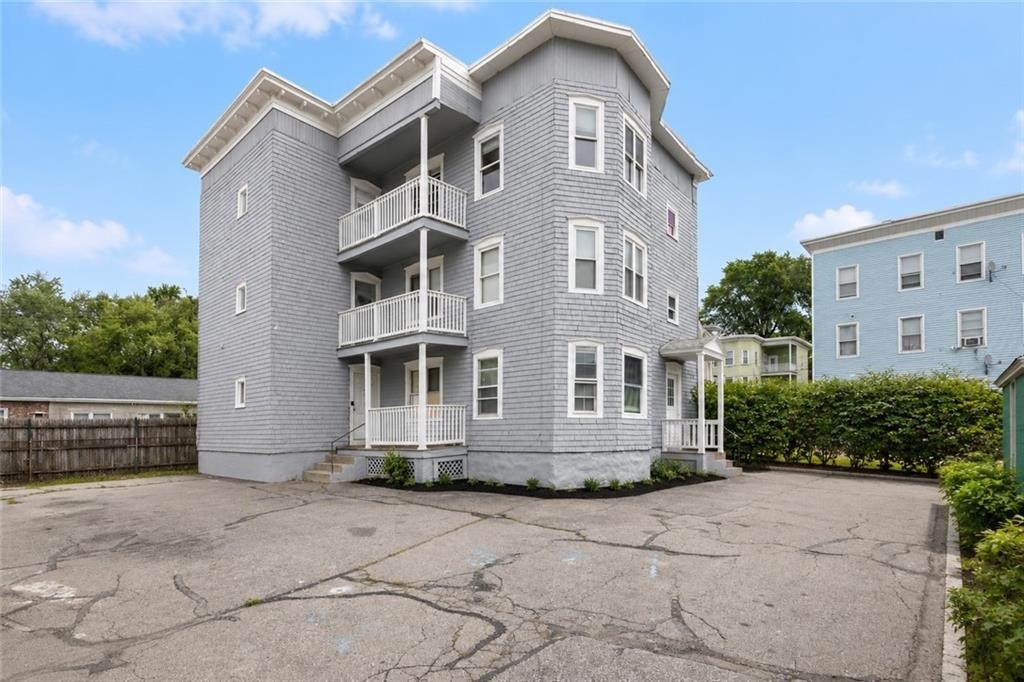 Gray multi-story residential building with three stacked balconies and a paved parking area.