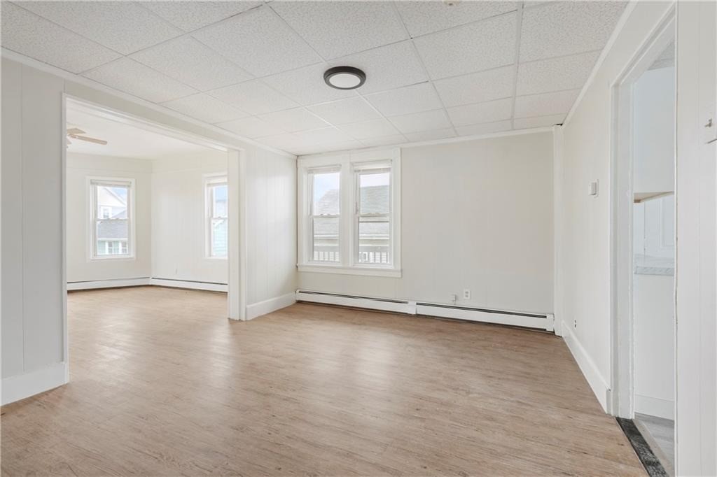 Vacant room with light wood-look flooring, two windows, and a wide opening to an adjoining room.
