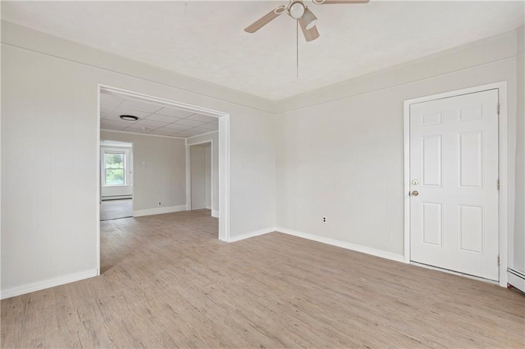 Empty room with light wood-look flooring, ceiling fan, and wide doorway to a windowed adjoining room.