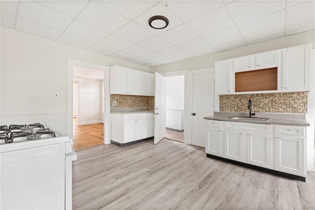 Vacant kitchen with white cabinets, mosaic tile backsplashes, and gray plank flooring.