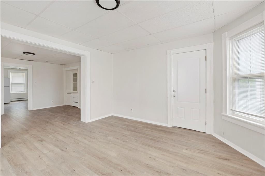 Empty living room with pale wood-look flooring, a large window, and an opening to an adjoining room.