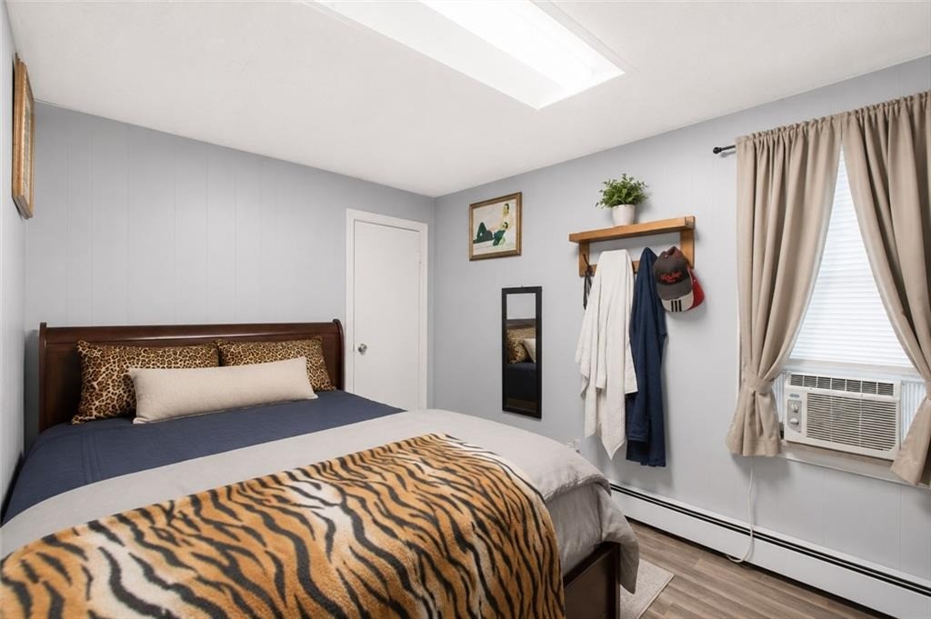 Bedroom with a dark wood bed, tiger-print blanket, window air conditioner, and coat hooks.
