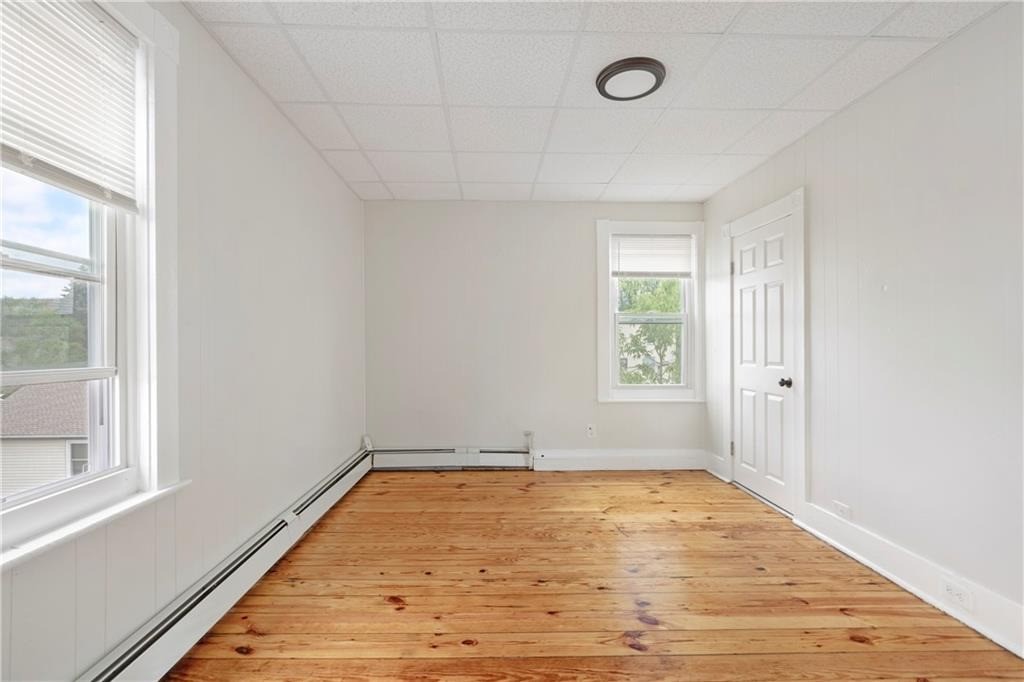 Empty room with warm hardwood floors, white paneled walls, and two windows.