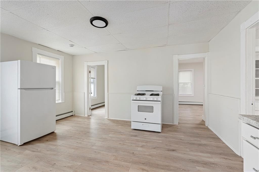 Empty kitchen with a freestanding stove, refrigerator, and light wood-look flooring.