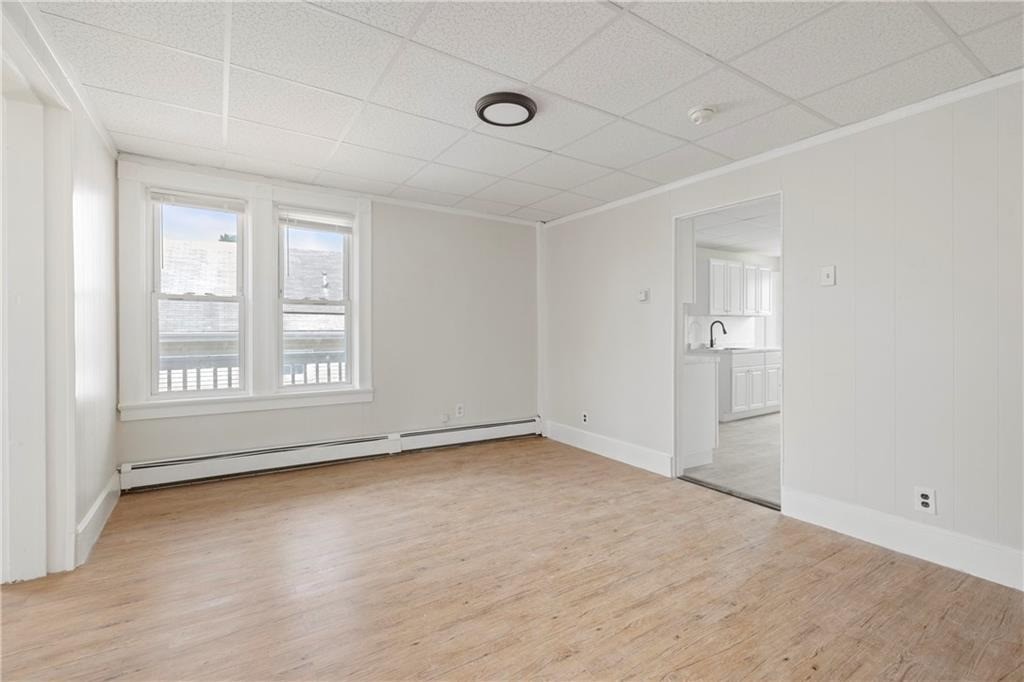 Empty room with light wood flooring, two windows, and a doorway into the kitchen.
