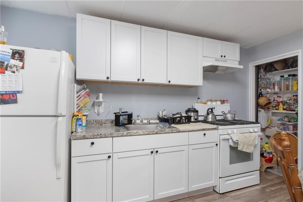 Kitchen with white cabinets, a granite-look counter, white appliances, and a stocked open pantry.