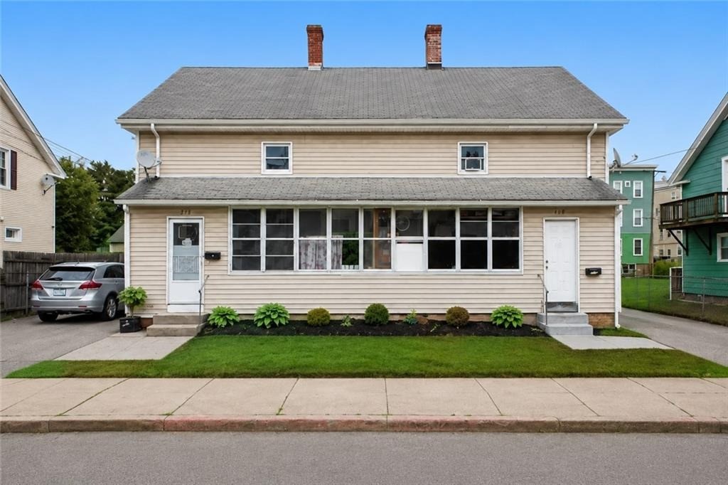 Beige two-story house with an enclosed front porch, two entrances, and a small lawn.