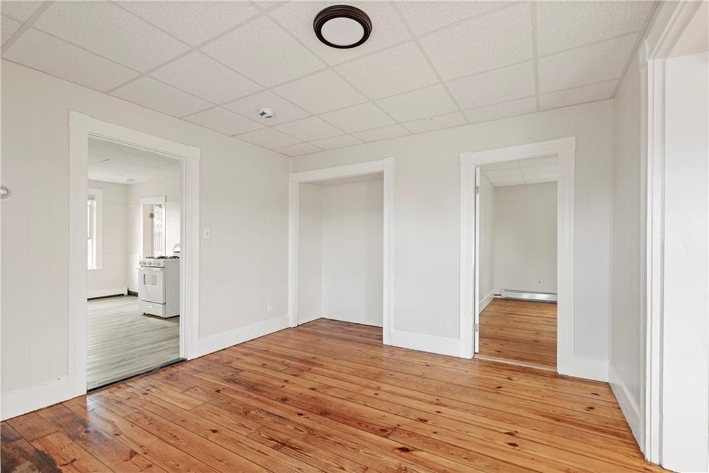 Vacant room with polished wood floors and doorways to a kitchen and adjoining room.