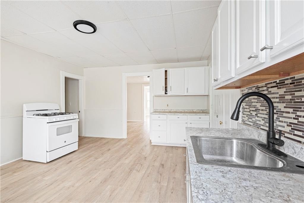 Kitchen with white cabinets, a freestanding stove, and a stainless steel sink beneath a black faucet.