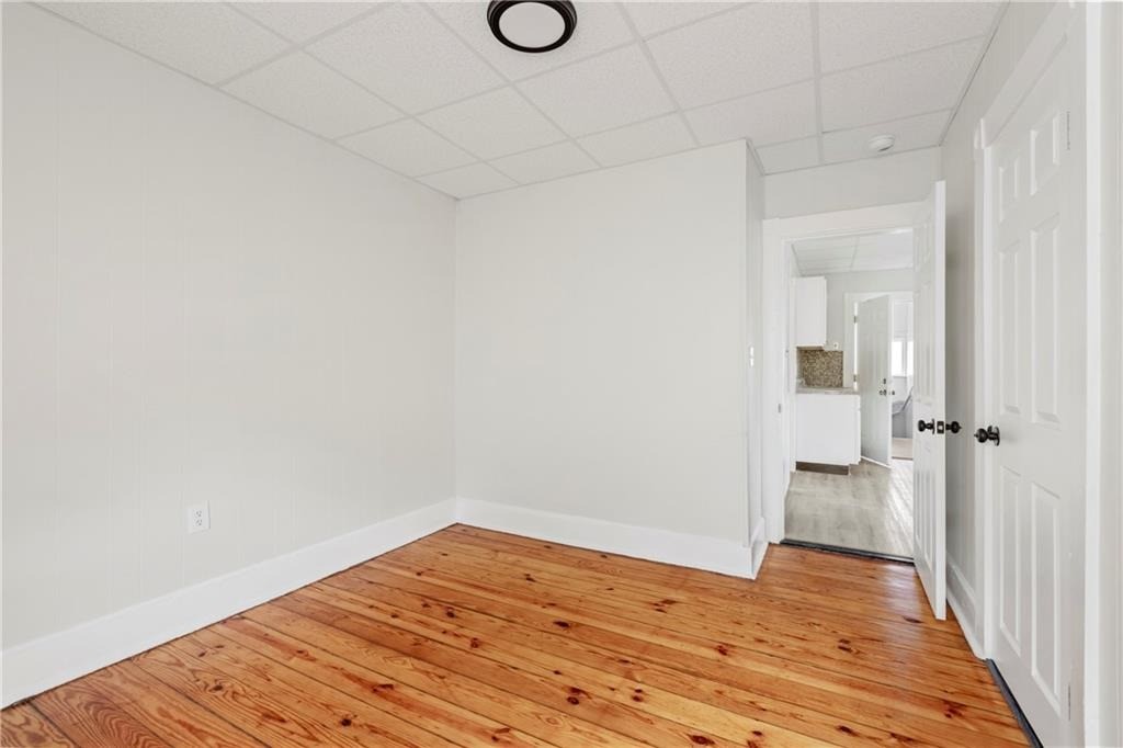 Empty room with plank hardwood floors and a doorway opening toward the kitchen.