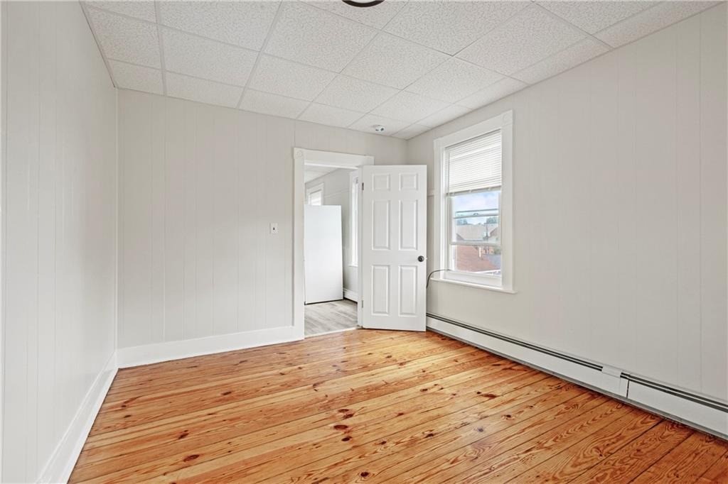 Empty room with polished hardwood floors, light paneled walls, and a window with blinds.