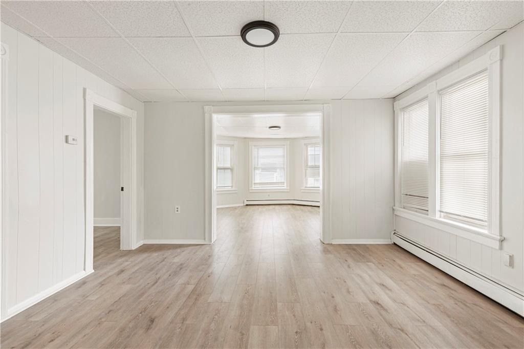 Empty room with light wood-look flooring and windows opening to a bay-window room.