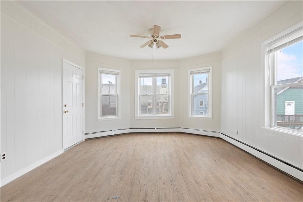 Empty bright room with light wood floors, white paneled walls, and a bay of windows.