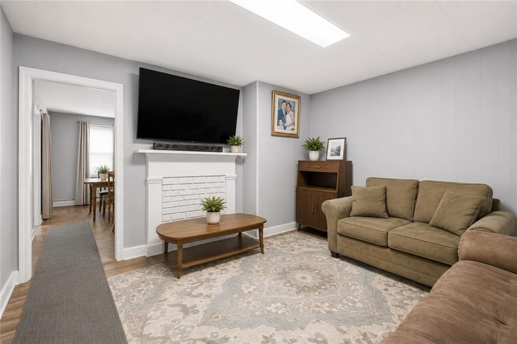 Living room with a beige sectional, patterned rug, white brick fireplace, and wall-mounted television.