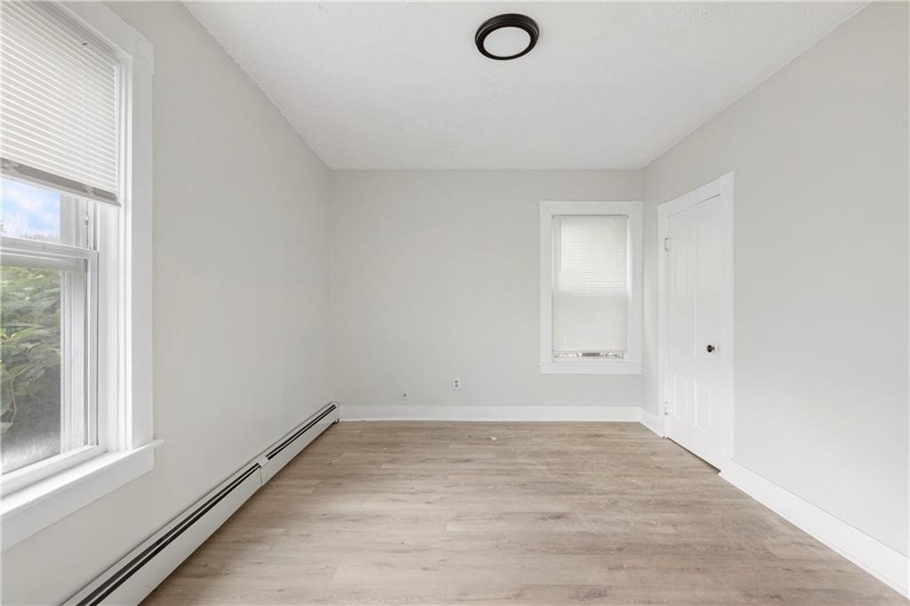 Vacant bedroom with two windows, light wood-look flooring, and a baseboard heater.