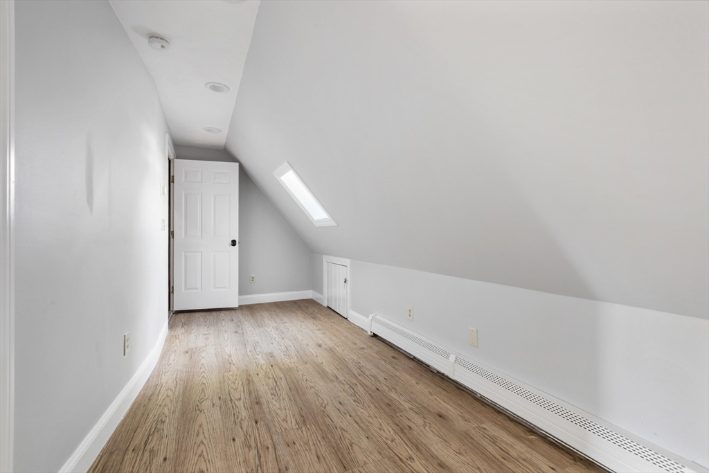 Finished attic room with a skylight, sloped ceiling, wood-look floors, and a long baseboard heater.