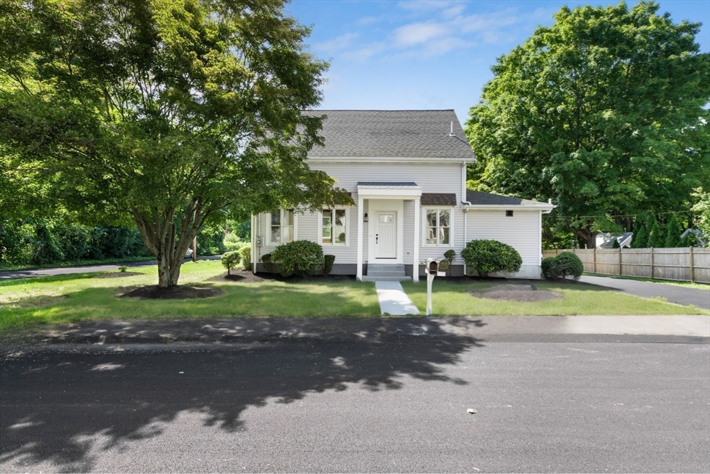 White-sided house with a covered entry, mature trees, shrubs, and a front lawn.