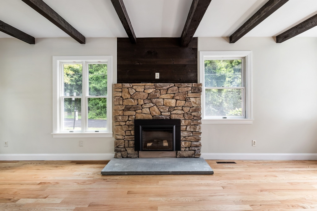Living room with a stone fireplace, exposed dark ceiling beams, and hardwood floors.