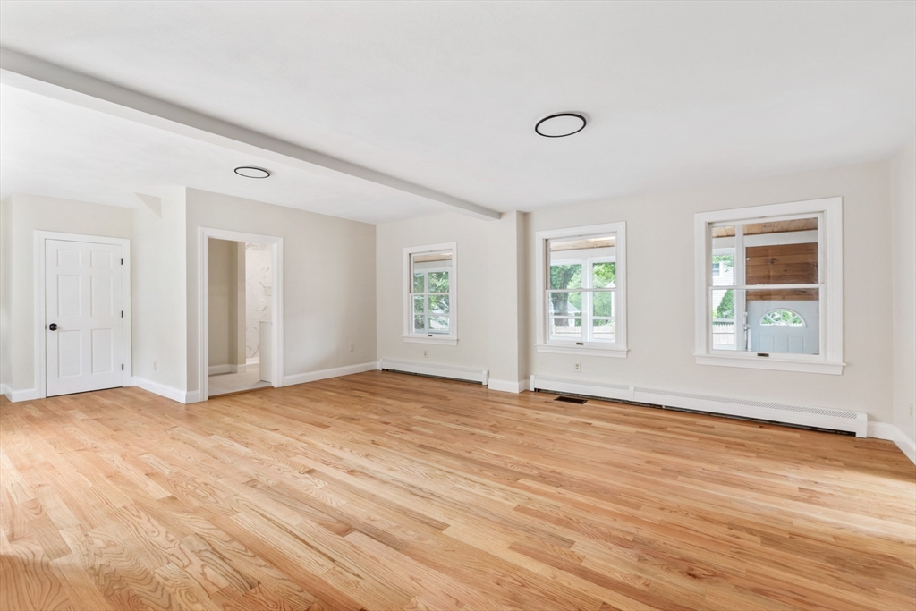 Empty living room with light hardwood floors, three windows, and recessed ceiling lights.