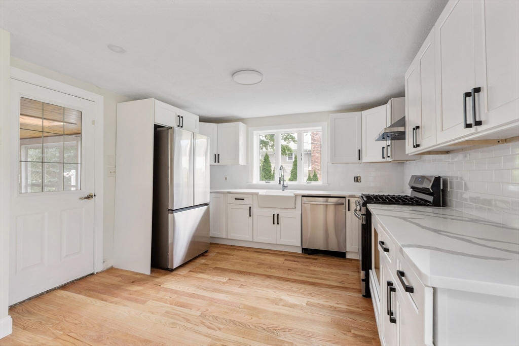 Kitchen with white shaker cabinets, stainless steel appliances, and a farmhouse sink beneath the window.