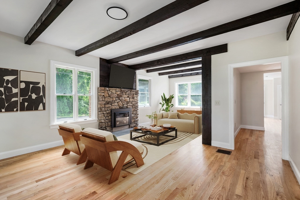 Bright living room with a stone fireplace, exposed dark beams, and hardwood floors.
