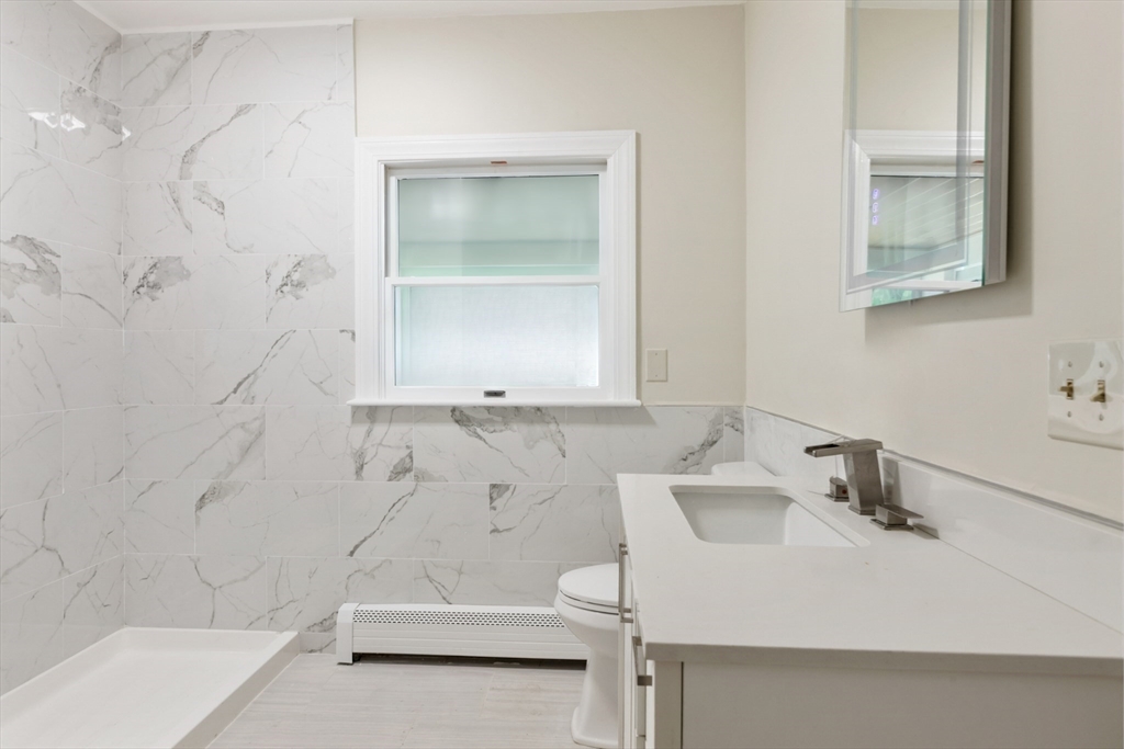 Bathroom with marble-look tile, a white vanity, and a window above the shower area.