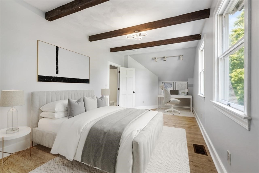 Bedroom with exposed ceiling beams, a large upholstered bed, and tall windows.