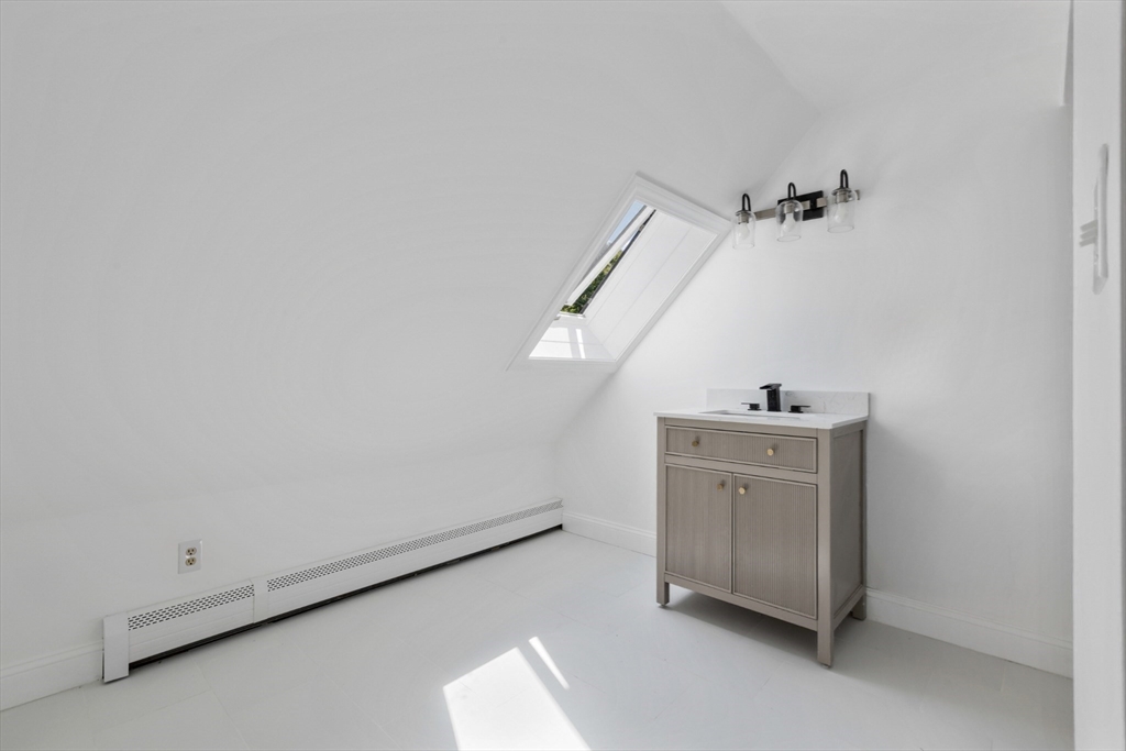 Attic bathroom with a freestanding vanity, skylight, sloped ceiling, and baseboard heater.