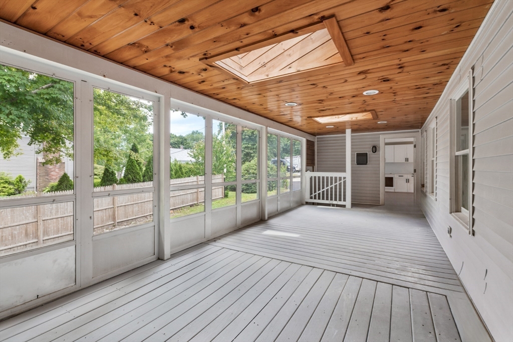 Enclosed porch with a wood ceiling, skylights, and windows overlooking a fenced yard.