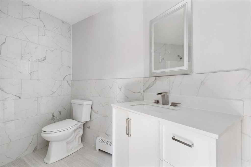 Bathroom with marble-look tile, a white toilet, and a modern vanity with chrome fixtures.